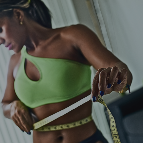 A woman is measuring her waist with a measuring tape while on a Semaglutide or Mounjaro or Phentermine weight loss management program at Zen Luxe Med Spa Aesthetic Services with Injector Resha